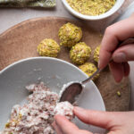 Creating little balls of goats cheese and prosciutto over a bowl next to completed appetizer rolled in pistachio