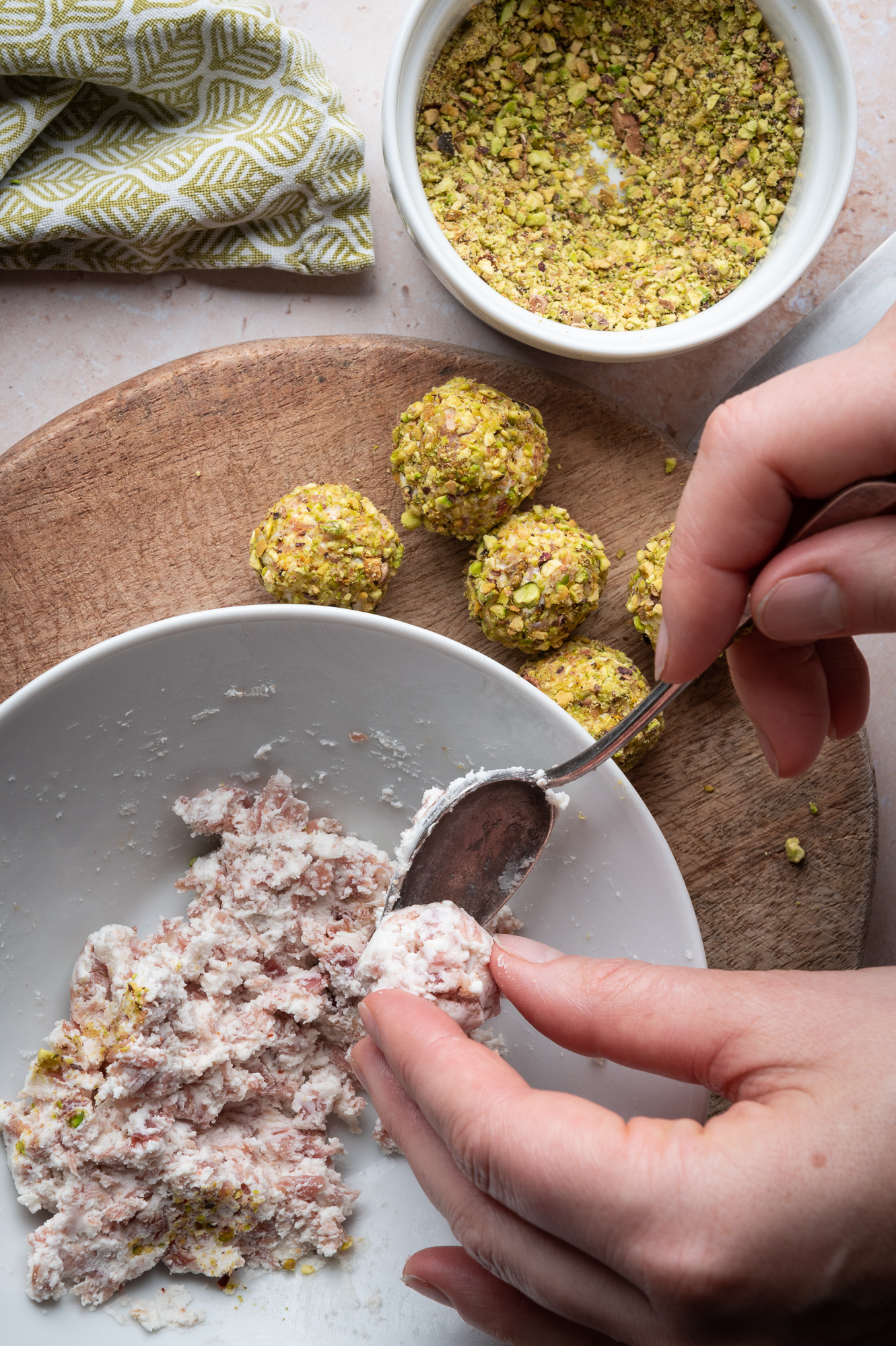 Creating little balls of goats cheese and prosciutto over a bowl next to completed appetizer rolled in pistachio
