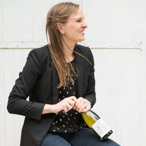 Sitting on a stool opening a bottle of white wine