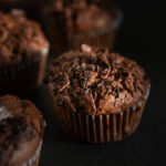 close up of chocolate zucchini muffins on a dark counter