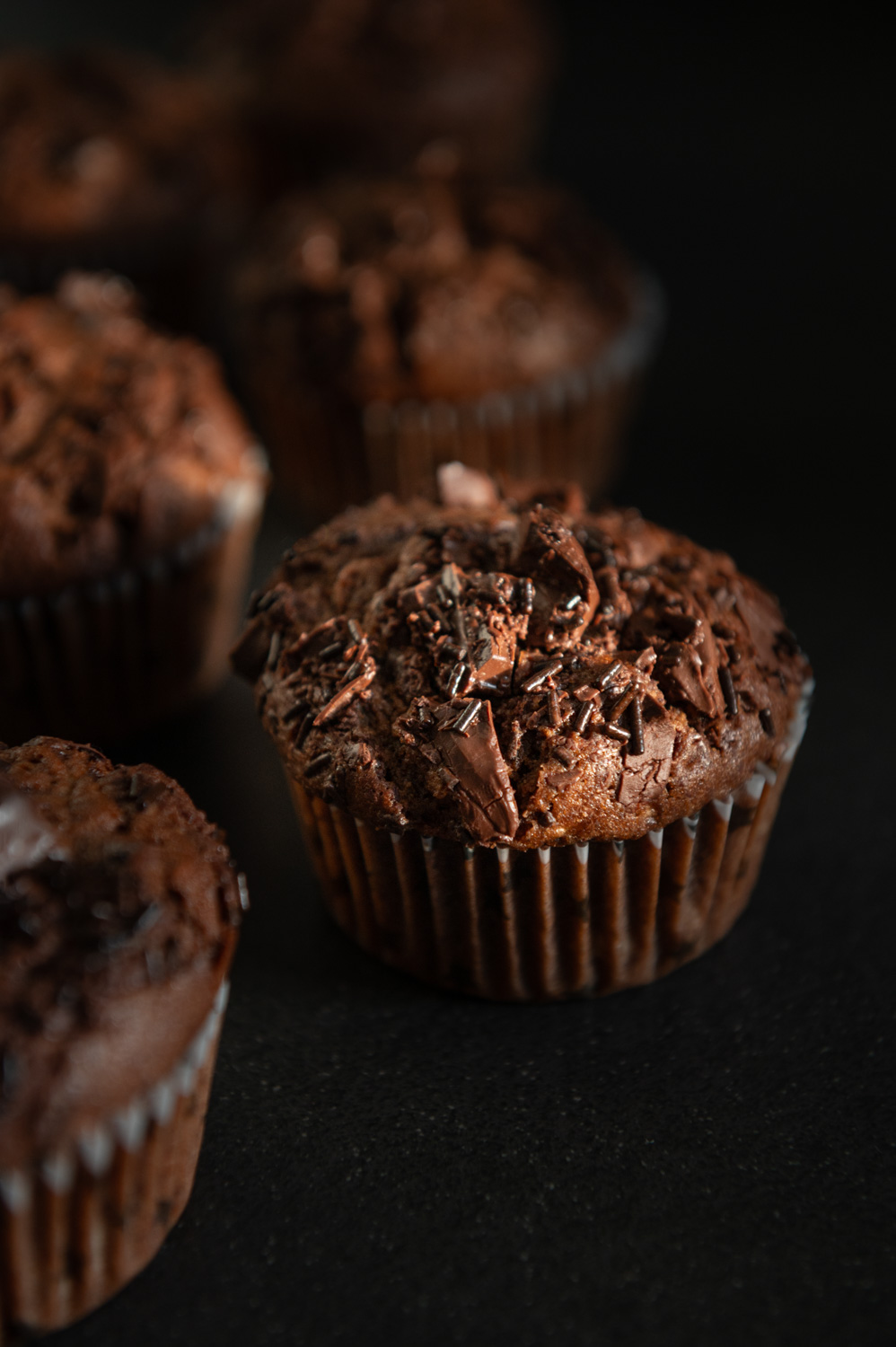 close up of chocolate zucchini muffins on a dark counter
