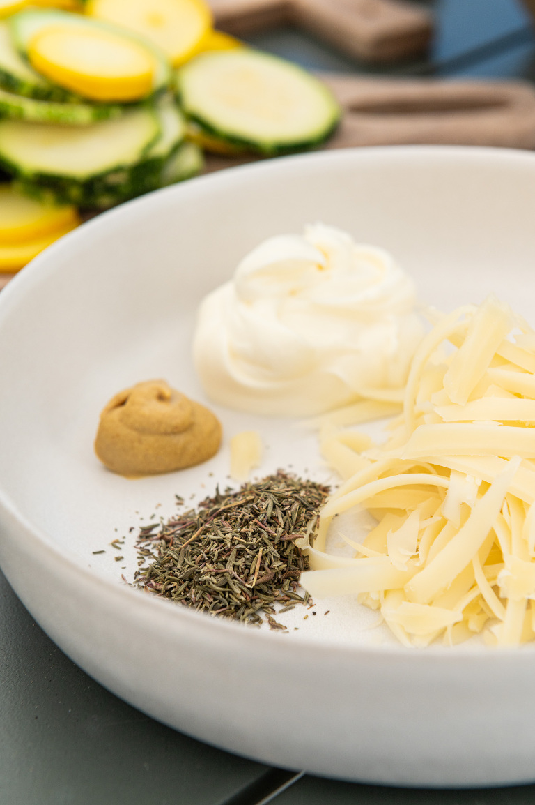 Bowl of ingredients for french courgette tart including thyme, mustard, creme fraiche and gruyere cheese