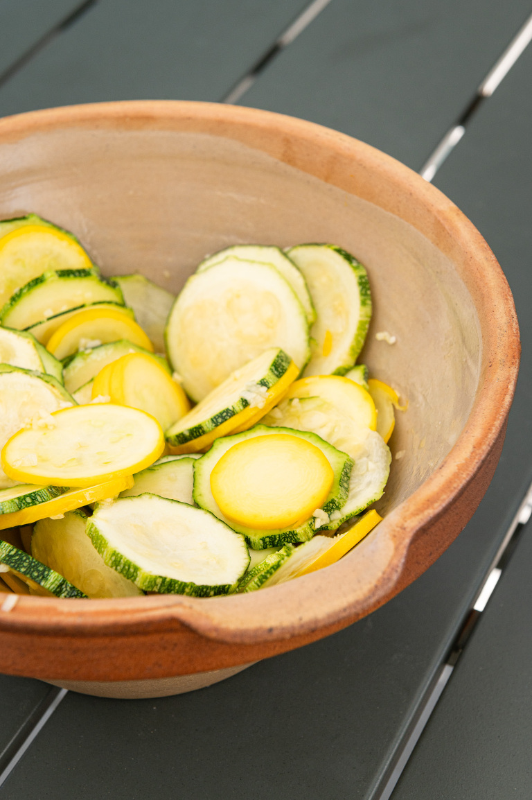 Bowl of slices yellow and romanesco courgettes in a rustic antique stoneware bowl on the patio table