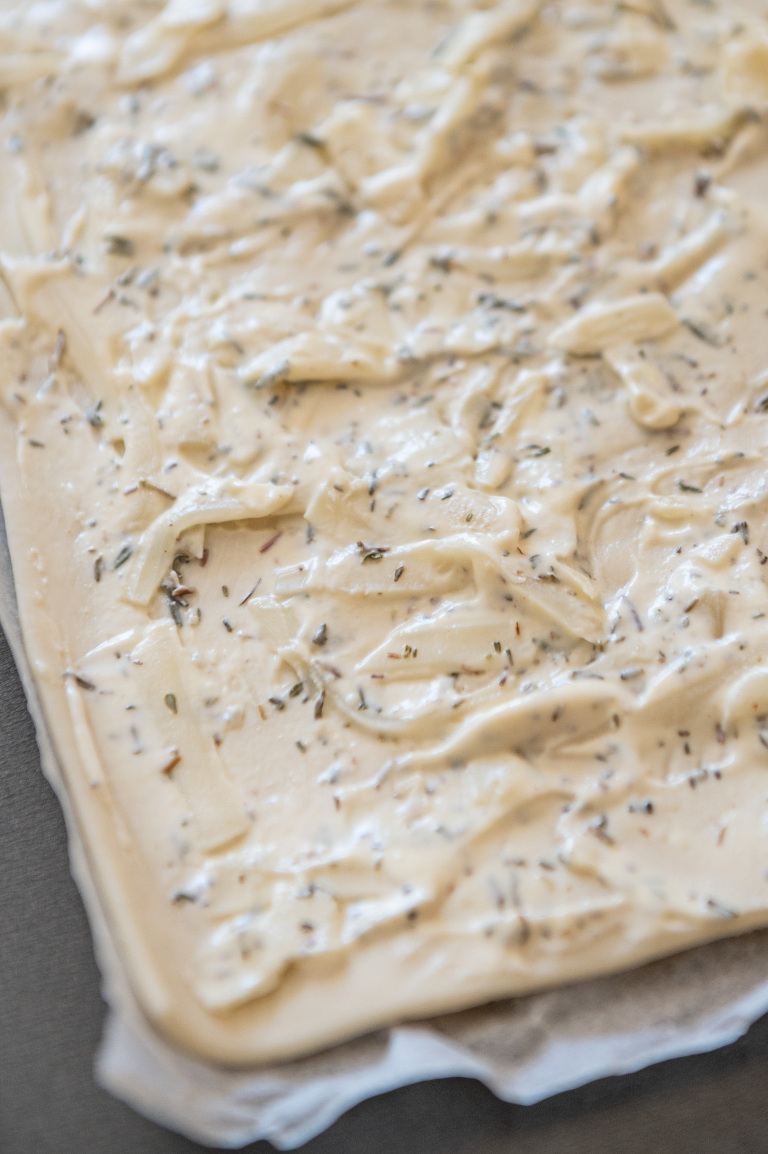 Puff pastry with thin layer of creme fraiche, thyme, mustard and gruyere cheese on a baking sheet