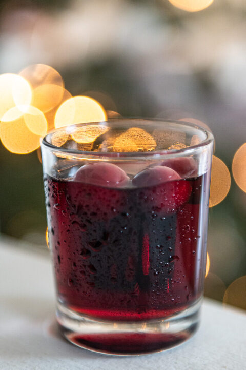 glass of sloe gin with frozen cranberries in front of bokeh light