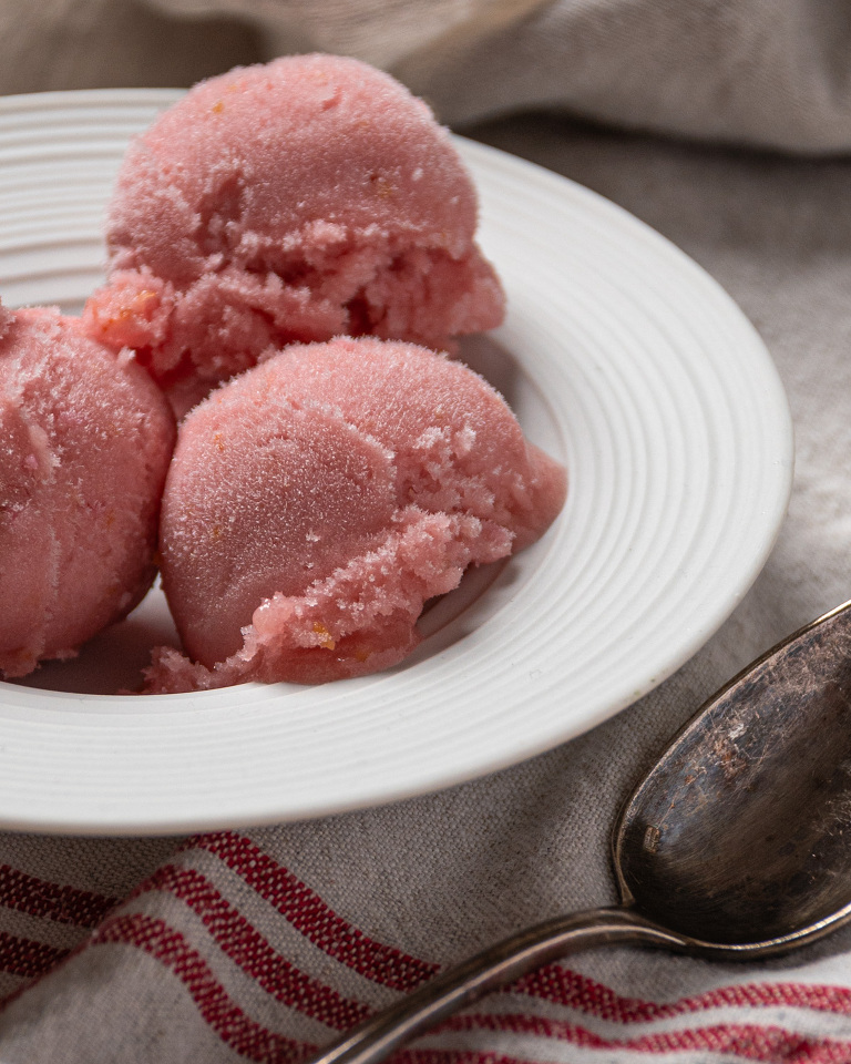Small white ceramic dish with three scoops of rhubarb elderflower sorbet on a linen tea towel