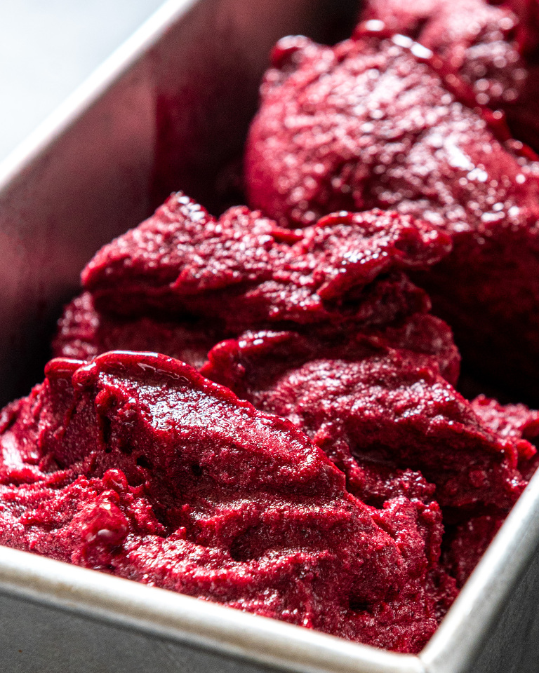 Metal container heaped with deep red black currant and elderflower sorbet
